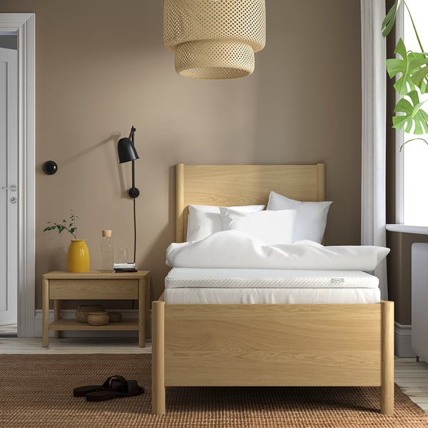 Bedroom with brown walls, wooden bed framed in light oak with white pillows and a yellow vase on nightstand.