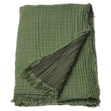 A VALLKRASSING throw blanket in green. Made of soft cotton with a crinkled texture and raw edges.