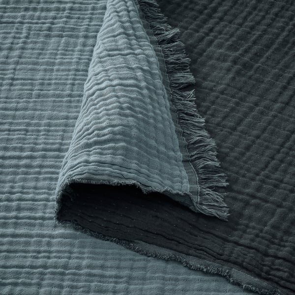 Soft, crinkled fabric with raw edges, likely made of cotton, draped over a dark surface. Textured, natural fibers showcase a woven design.