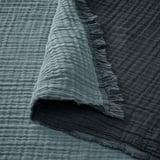 Soft, crinkled fabric with raw edges, likely made of cotton, draped over a dark surface. Textured, natural fibers showcase a woven design.