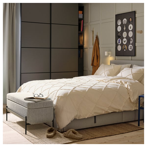 Cozy bedroom with white bedding, black frame bed, gray wardrobe, beanie, slippers, and wall art.