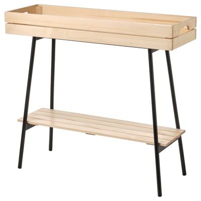 The VANILJSTÅNG plant stand in light wood with black metal legs. It has a rectangular wooden tray top and a bottom shelf for storage or display.