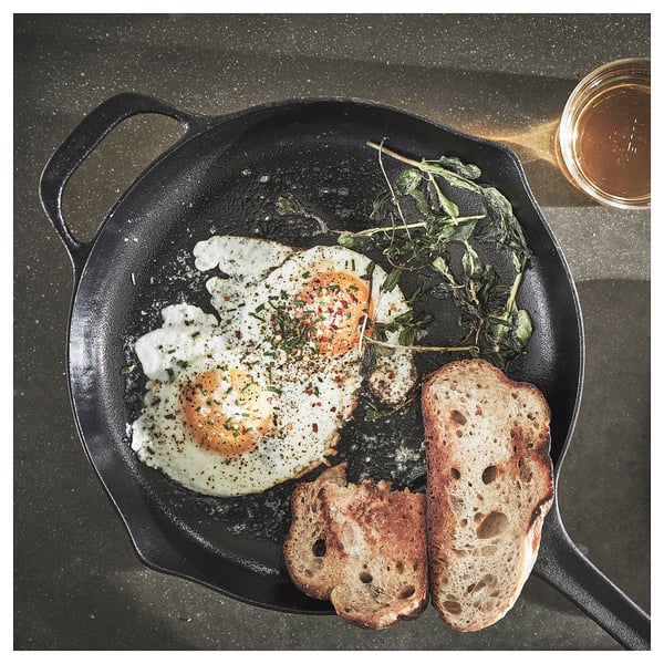 Black cast-iron skillet with fried egg, greens, and toast. Seasoned with herbs and spices.