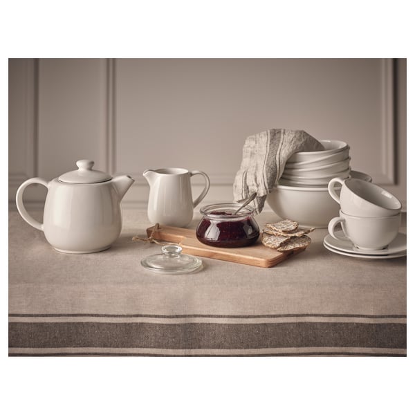 White ceramic tea set on brown tablecloth. Includes teapot, creamer, cups, and bowl. Simple, round design.