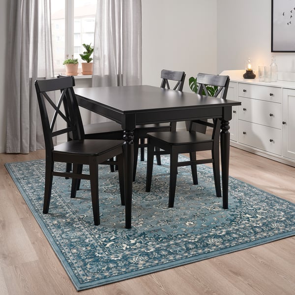 Blue floral rug under black dining table with chairs.