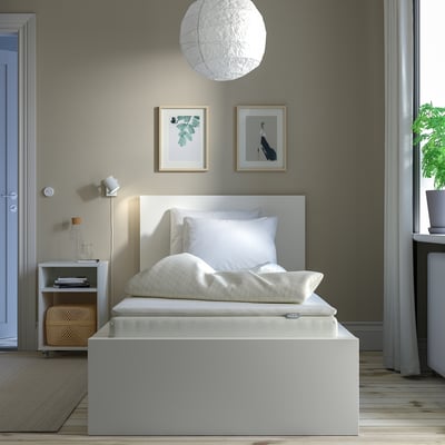 Modern bedroom with VESTERÖY mattress, white bedding, green wall, art, pendant light, bedside table, books, basket, window, curtains, plant.