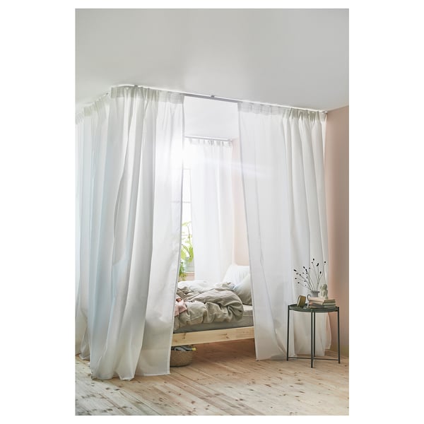 Minimalist bedroom with sheer curtains, cozy bed, and side table with books and a vase.