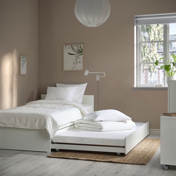 Modern minimalist bedroom with VIHALS white daybed & trundle. Large white pillows, hanging light, wall art, and window with view. Clean and spacious.