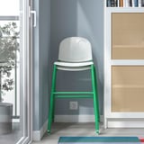 A white and green junior chair placed in a room, ideal for kids to sit at a table, with stackable and anti-slip.