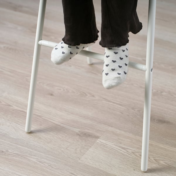 White junior chair with someones feet in socks patterned with black hearts resting on it.