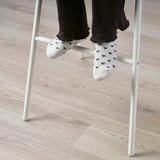 White junior chair with someones feet in socks patterned with black hearts resting on it.