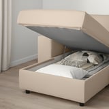 Beige sofa-bed with storage open, showing folded bedding and pillows inside.