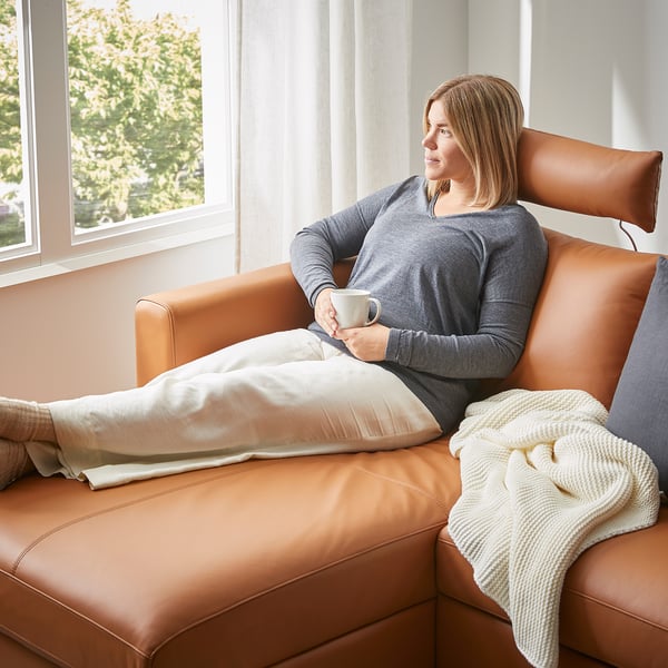 Woman relaxes on tan VIMLE sofa, drinking from a mug. Cozy, comfortable living room setting.