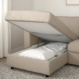 Beige sofa with open storage compartment showcasing white bedding, demonstrating its hidden bed function.