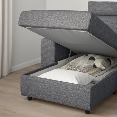 A gray fabric sofa bed with storage compartment open, revealing folded blankets and pillows.