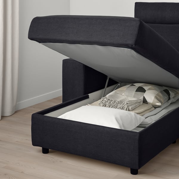 Dark sofa with storage and bed function open, revealing pillows and blanket.
