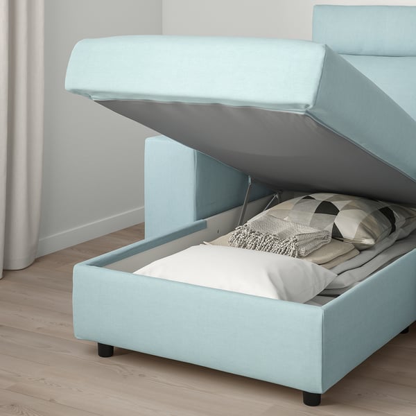 Light blue sofa with storage under seat, open to show blankets and pillows.