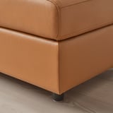 Brown leather sofa leg detail; stiff, quality leather, sturdy black metal base, polished wooden floor backdrop.
