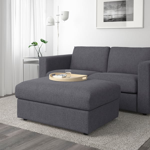 Modern gray sectional sofa with ottoman, wooden tray, and side lamp. Storage and drink holder.