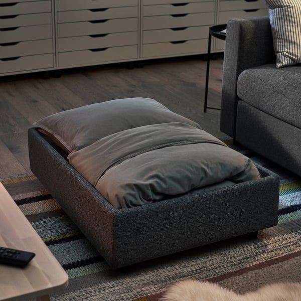 Gray VIMLE footstool on striped rug beside wood floor sofa.