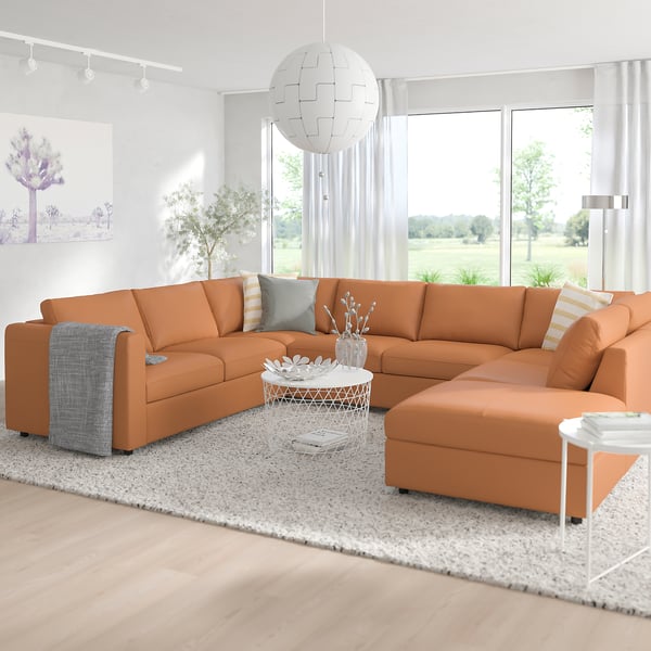 Modern orange l-shaped VIMLE sofa with cushions, centered in a bright, minimalist living room. Large window, white curtains, rug, and coffee table.