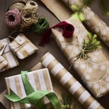 Gift wrapping scene with brown paper, white snowflake designs, green and red ribbons, and pine branches.