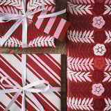 Three vibrant red gift boxes wrapped in festive, patterned paper tied with elegant white ribbons.