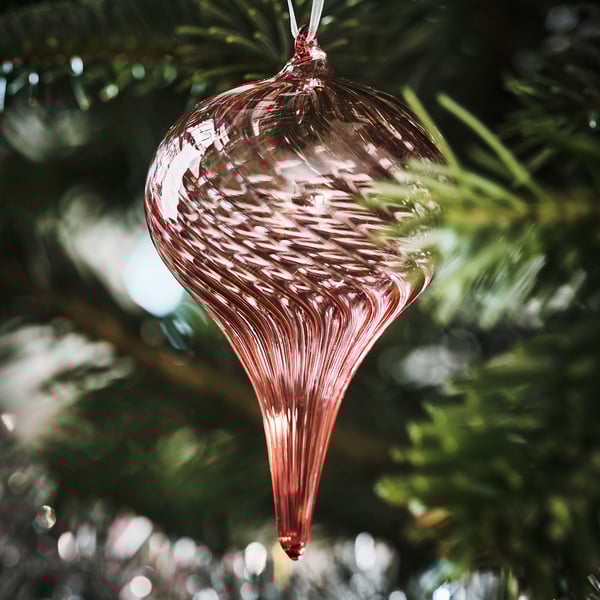 Glass christmas ornament hangs on a tree, with beautiful red swirls and clear sections, reflecting light, making it sparkle.
