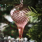 Glass christmas ornament hangs on a tree, with beautiful red swirls and clear sections, reflecting light, making it sparkle.