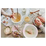 Busy kitchen scene with people baking, using mixing bowls and various ingredients on a countertop.