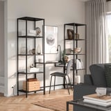 Black VITTSJÖ shelves and desk with books, decor, plants, and lamp. Gray couch.