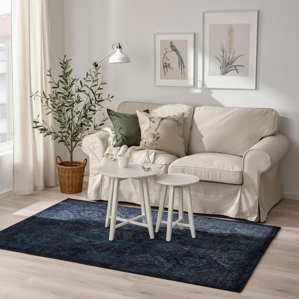 Beige sofa, small tables, blue rug, green cushions, wall art.
