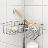 Metal shower caddy with soap and brush resting against white tiled wall.