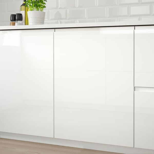 Modern kitchen with white high-gloss VOXTORP cabinets, featuring integrated handles. A potted plant and a bottle rest on the countertop.
