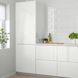 A modern white kitchen with glossy VOXTORP cabinets and backsplash. Potted plants and olive oil bottle are placed on the countertop.