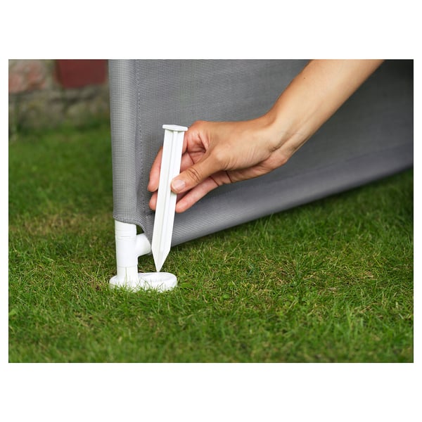Hand placing white plastic stake into grassy area against gray mesh structure.