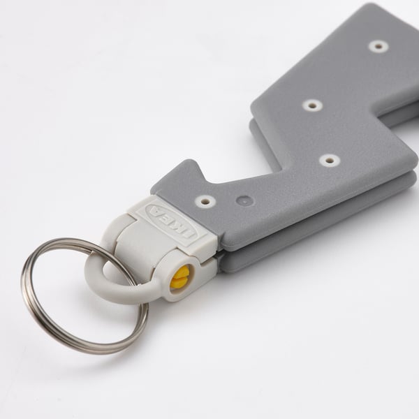 Gray phone holder keychain, folded, quality plastic and metal ring, ikea logo visible.