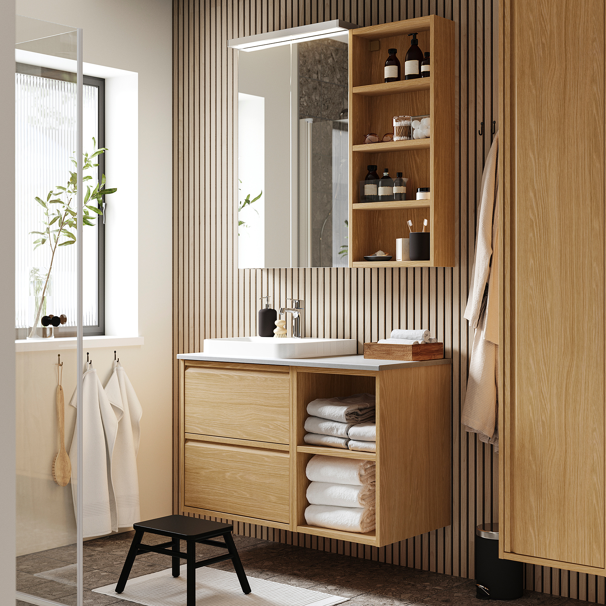 Modernes Badezimmer mit hellem Holzwaschtisch ÄNGSJÖN, Waschbecken aus weißem Marmor, großem Spiegel, offenen Regalen und hängenden Handtüchern.