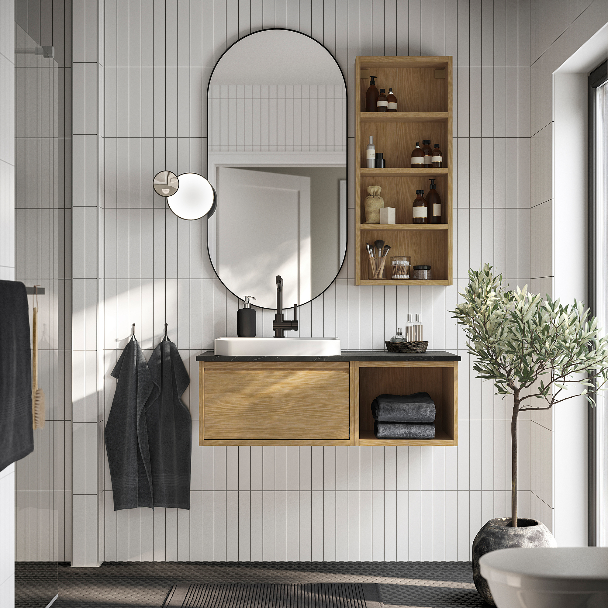 Modernes Badezimmer mit hellem Holzwaschtisch, weißem Waschbecken, rundem Spiegel, dunklen Handtüchern und Pflanze.