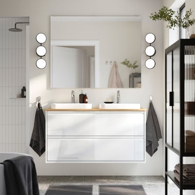 Ein modernes weißes ÄNGSJÖN-Badezimmer mit elegantem Waschtisch, Doppelwaschbecken, Bambusplatte, Spiegeln, dunklen Handtüchern und schwarzer Dusche.