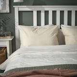 Beige ÄNGSLILJA Kissenbezüge aus Baumwolle auf dem Bett mit weißem Kopfteil, Bettdecke, brauner Überwurf.