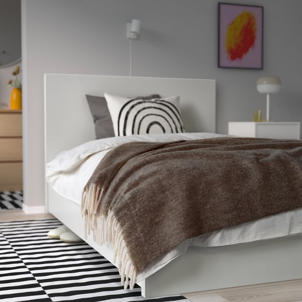 Kuscheliges Bett mit großer grauer ALLFRAKEN Wolldecke, Regenbogenkissen, schwarz/weißem Teppich, Seitenlampe.