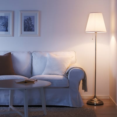 Gemütliches Wohnzimmer mit hellblauer ÅRSTID-Lampe, weißem Schirm, der weiches Licht in der Nähe eines hellblauen Sofas und eines Couchtisches bietet.