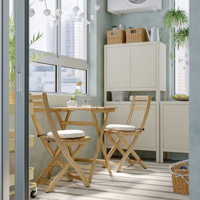 Esszimmergarnitur aus Holz mit gepolsterten Stühlen am Fenster, die einen kompakten Raum mit Schränken und Pflanzen bietet.