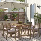 Akazien-Esszimmergarnitur mit 4 gepolsterten Stühlen, Teppich, Obstschale, Zaun, Pflanzen, Sonnenschirm.