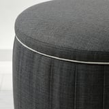 Runder, dunkelgrauer gepolsterter Fußhocker mit genähten Kanten, der hochwertigen Stoff und Design zeigt.