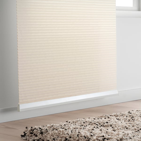 Beigefarbenes Rollo, Fenster teilweise abdeckend. Beige gesprenkelter Teppich auf Holzboden.