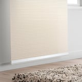 Beigefarbenes Rollo, Fenster teilweise abdeckend. Beige gesprenkelter Teppich auf Holzboden.