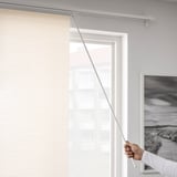 Eine Person zeichnet einen durchsichtigen Paneelvorhang über ein großes Fenster, das die Privatsphäre erhöht und gleichzeitig natürliches Licht in einen minimalistischen Raum lässt.