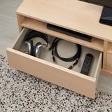 Schublade mit heller TV-Bank aus Holz bietet Platz für Kopfhörer, Kabel und Fernbedienung.